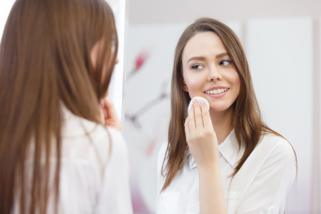attractive woman looking at a mirror cleanses the face with a cotton pad after a shower