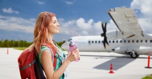 Young woman with a backpack walking to a plane while holding a water bottle.