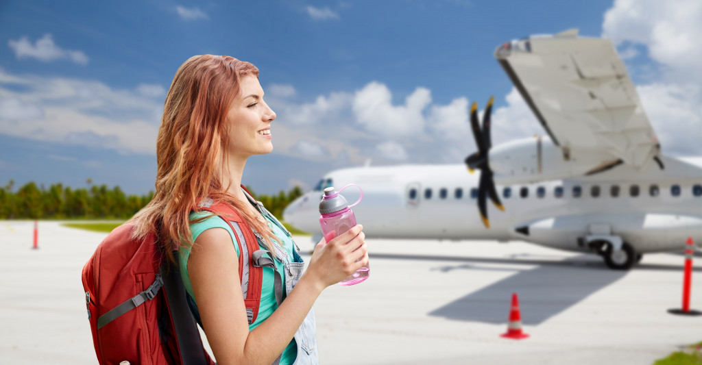 Young woman with a backpack walking to a plane while holding a water bottle.