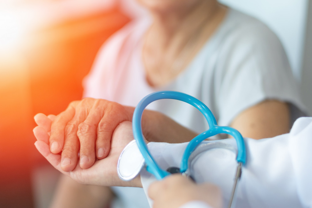 elderly woman holding hand of doctor with stethoscope
