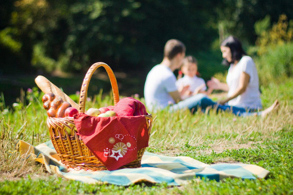 family having picnic in the grass with basket of food and blanket in the foreground