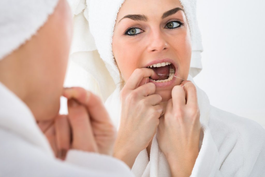 woman flossing teeth in front of mirror