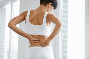 a woman holding her back with both of her hands